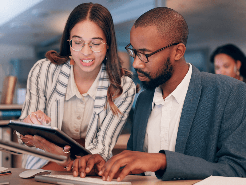 Two people working together in an office with a tablet and a laptop.